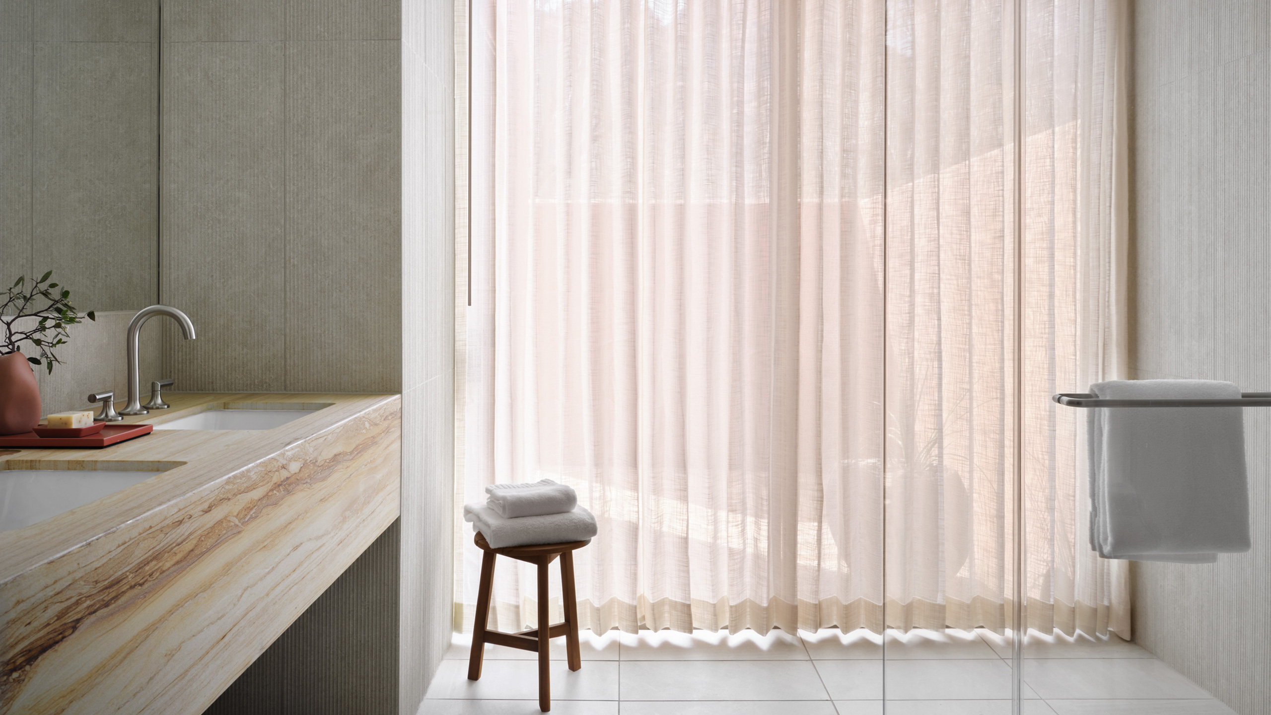 Glass shower with light coming in sheer curtains and stool near window